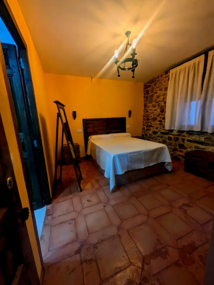 Dormitorio con cama de matrimonio, vigas de madera y ventana con vistas a la Sierra del Alto Rey